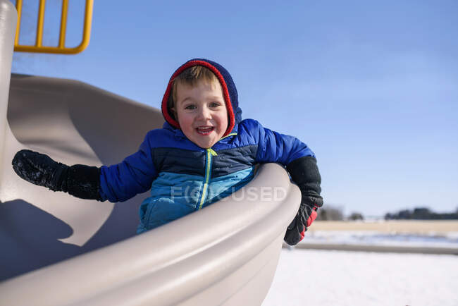 Bambino sorridente che scivola giù da uno scivolo — Foto stock