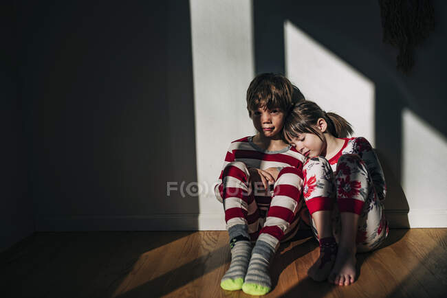 Brother and sister sitting on the floor in their pyjamas — Stock Photo