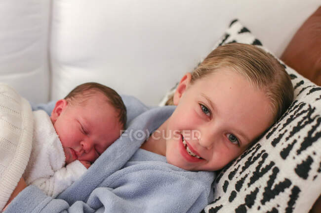 Smiling girl lying on couch with her baby sister — Stock Photo