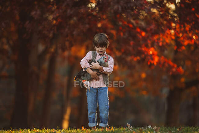 Garçon debout à l'extérieur câlinant un poulet, États-Unis — Photo de stock