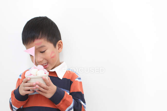 Menino com um beijo de batom no rosto segurando uma tigela de marshmallows — Fotografia de Stock