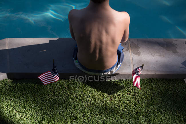 Хлопчик сидить на краю басейну біля американських прапорів. — стокове фото
