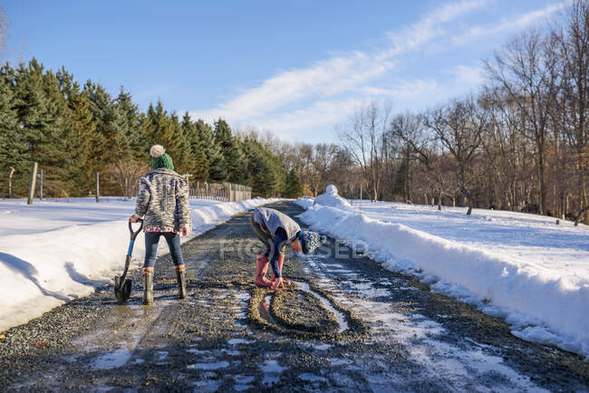 Niño y niña jugando en el camino en la nieve derretida - foto de stock