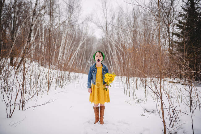 Chica de pie en la nieve sosteniendo un ramo de flores y bostezos - foto de stock