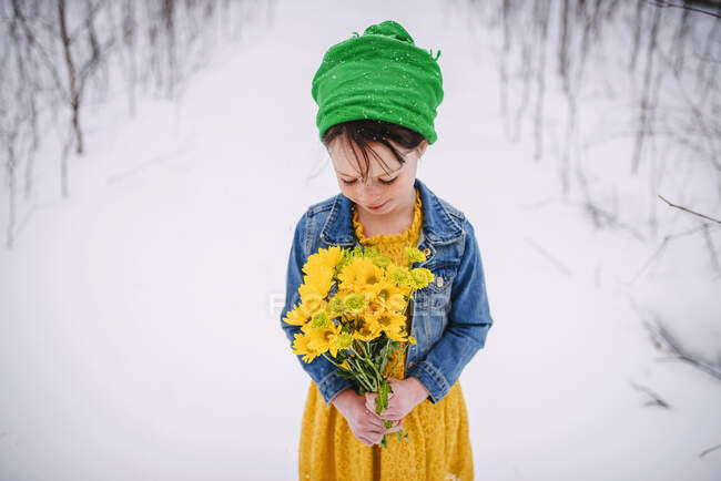 Menina de pé na neve segurando um monte de flores — Fotografia de Stock