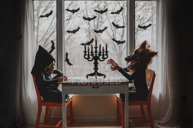Two children in Halloween costumes sitting by a window doing a puzzle, United States — Stock Photo