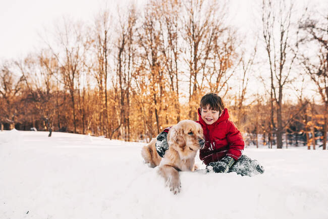 Menino sentado na neve com seu cão golden retriever — Fotografia de Stock
