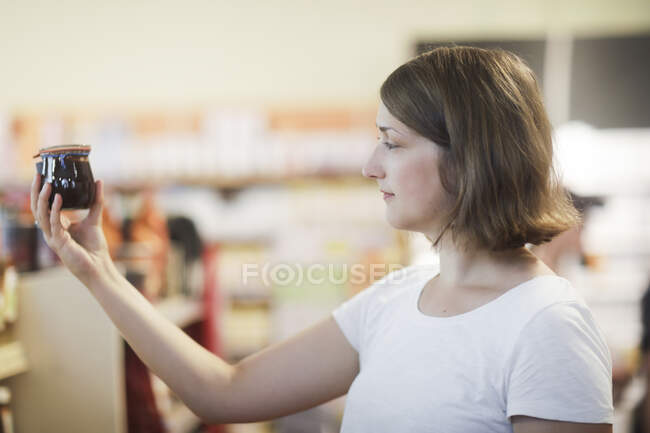 Woman standing in a supermarket aisle holding a pot of jam — Stock Photo