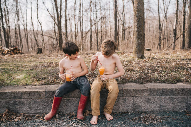 Dos chicos sentados en una pared disfrutando de una bebida de verano - foto de stock