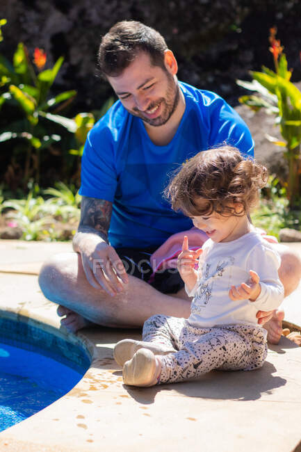 Father and daughter sitting by the edge of a swimming pool, Brazil — Stock Photo