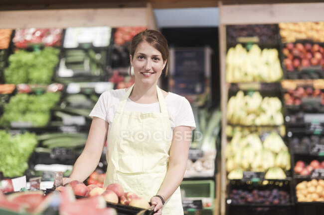 Retrato de um assistente de vendas sorridente em pé na seção de frutas e vegetais — Fotografia de Stock
