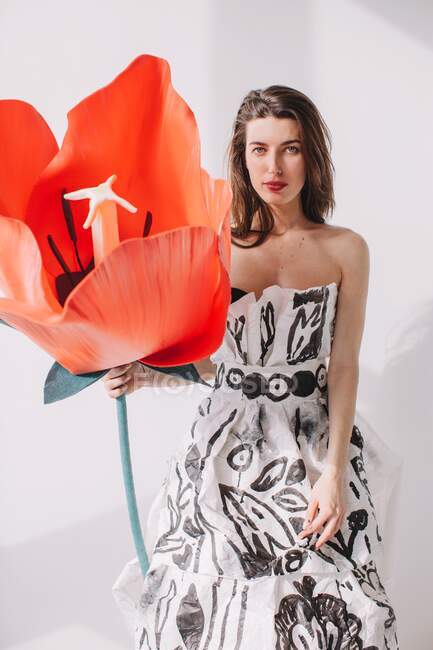 Mulher usando um vestido de papel segurando uma tulipa artificial — Fotografia de Stock