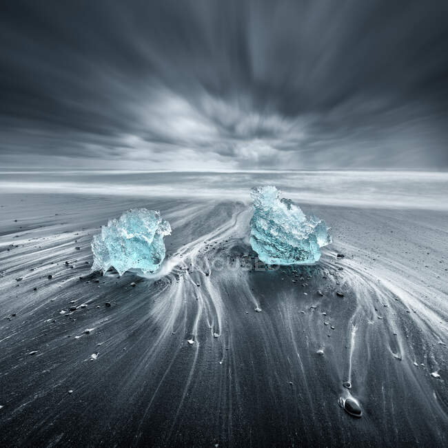 Маленькие айсберги на черном песчаном пляже в облачный день — стоковое фото
