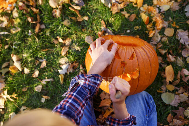 Overhead view of a Boy carving a Halloween pumpkin in the garden, United States - foto de stock