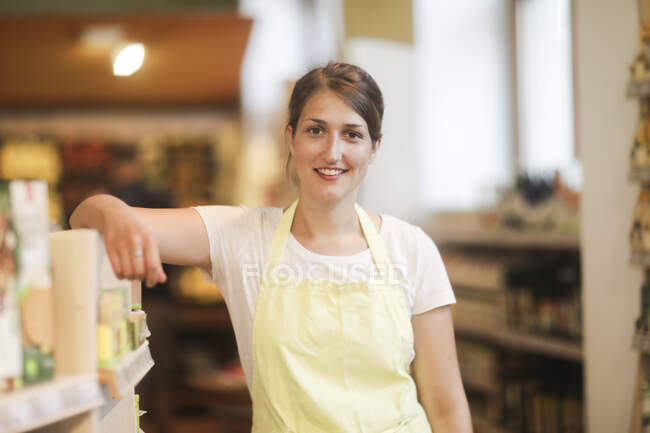 Portrait of a Smiling sales assistant leaning against a shelf in a shop — Stock Photo