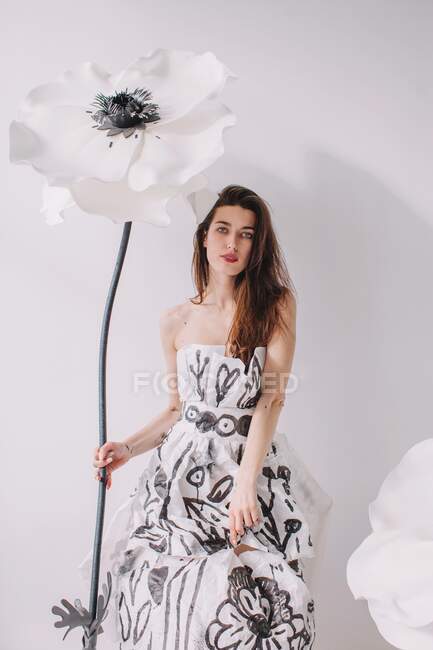 Женщина в бумажном платье, стоящая рядом с искусственными цветками анемона — стоковое фото