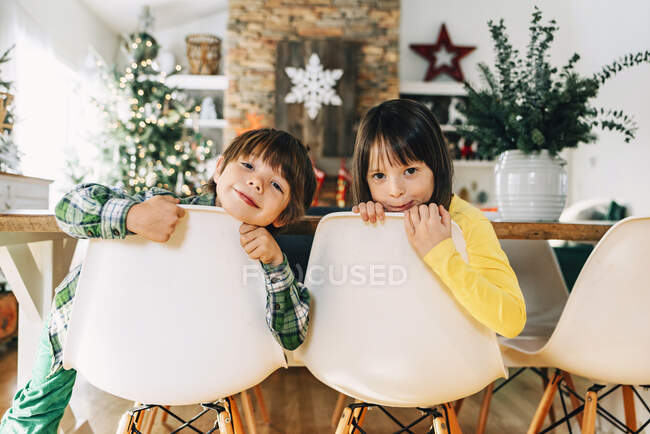 Brother and sister sitting on dining room chairs at Christmas — Stock Photo