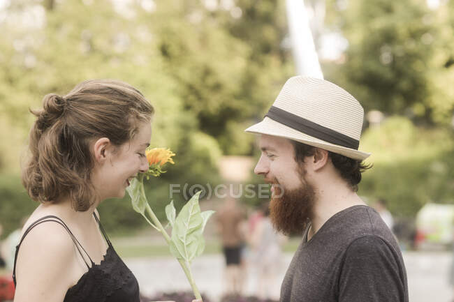 Man standing in a park giving his girlfriend a sunflower — Stock Photo