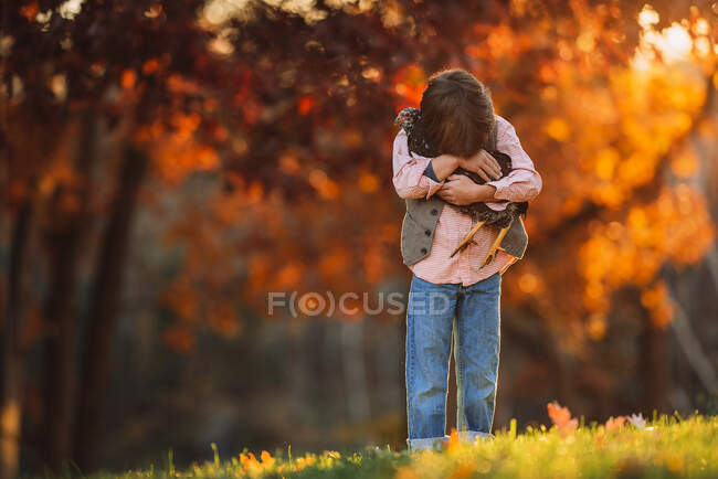 Хлопчик, що стоїть надворі, обіймає курку, Сполучені Штати Америки. — стокове фото