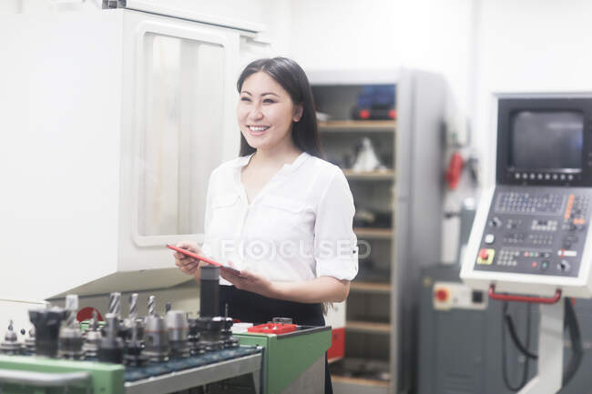 Porträt einer Ingenieurin, die Geräte in einer Werkstatt bedient und dabei ein digitales Tablet hält — Stockfoto