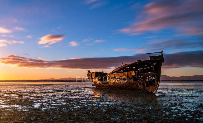 Разрушенная лодка на закате над морем — стоковое фото