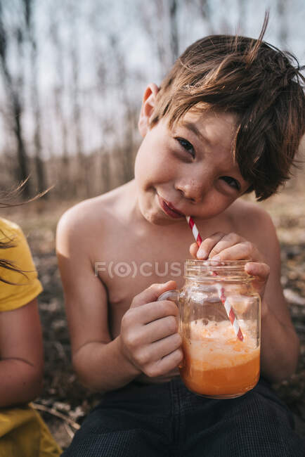 Lächelnder Junge, der im Sommer einen orangefarbenen Wagen trinkt — Stockfoto