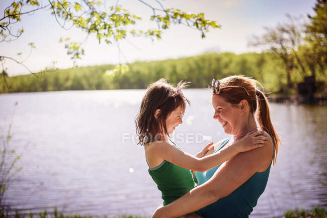 Mãe em pé junto a um lago carregando sua filha — Fotografia de Stock