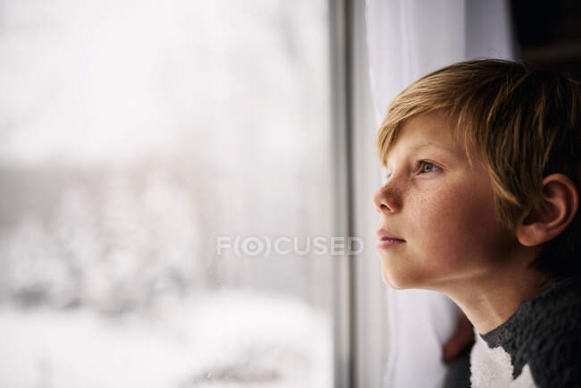 Junge schaut im Winter aus dem Fenster — Stockfoto
