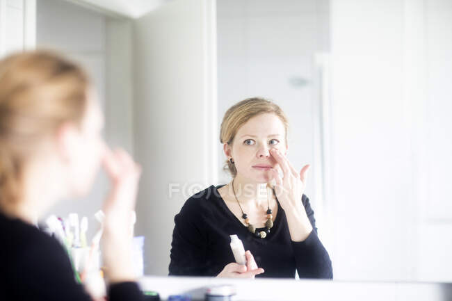 Жінка стоїть у ванній, застосовуючи макіяж — стокове фото