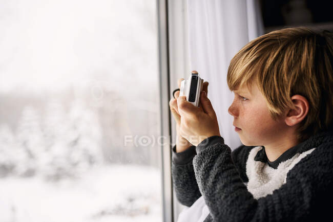 Boy sitting by a window taking a photo with a pocket camera — Stock Photo