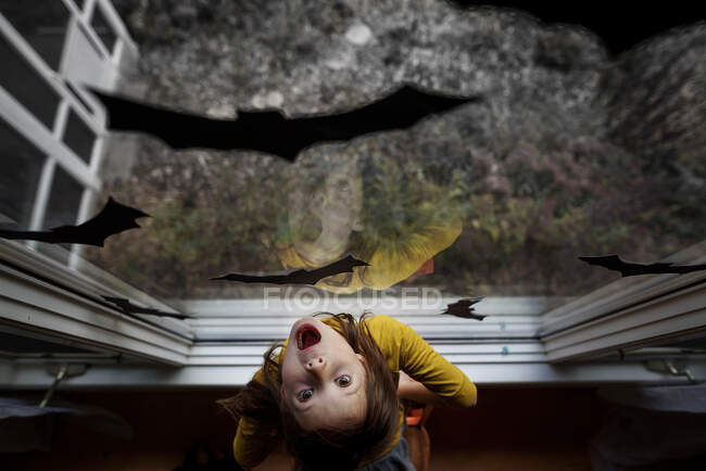 Blick auf ein Mädchen, das an einem Fenster steht, das zu Halloween mit Fledermausdekorationen dekoriert ist, Vereinigte Staaten — Stockfoto