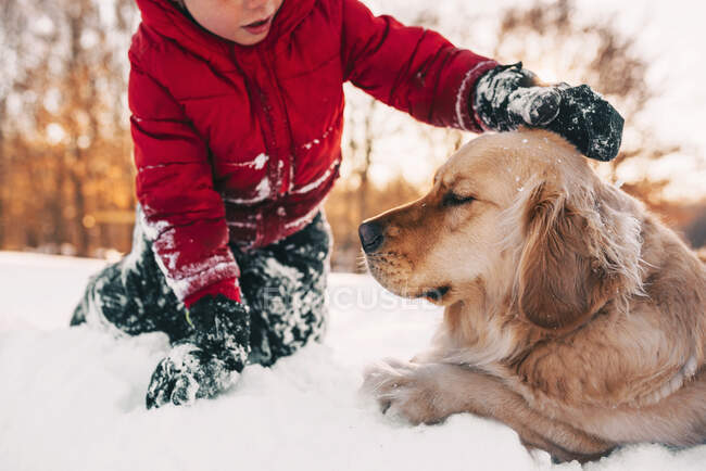 Boy sitting in the snow with his golden retriever dog — Stock Photo