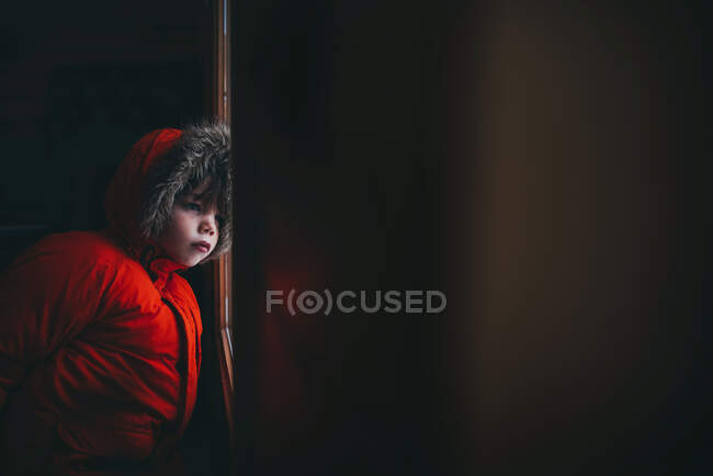 Хлопчик у зимовій куртці, що стоїть біля вхідних дверей — стокове фото