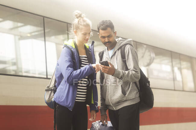 Couple standing on a train platform looking at a mobile phone — Stock Photo