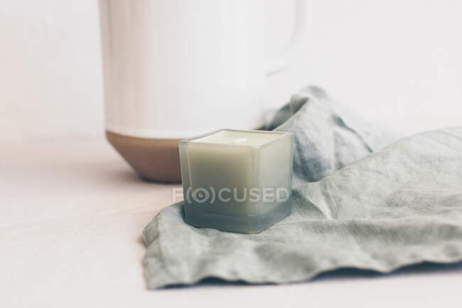 Candle on linen napkin next to a jug — Stock Photo