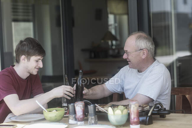 Père et fils adultes assis sur la terrasse pour porter un toast de fête — Photo de stock