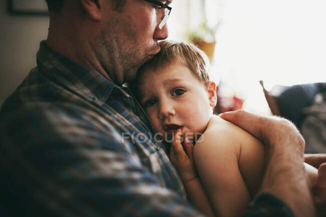 Père assis sur le canapé câlinant son fils et l'embrassant sur la tête — Photo de stock