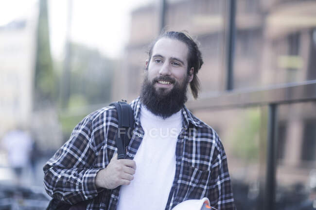 Sorrindo homem andando pela rua carregando um capacete de segurança — Fotografia de Stock