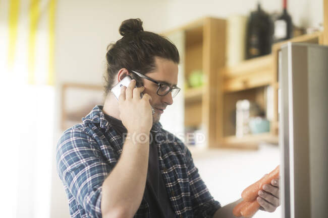 Portrait of a man holding carrots talking into a mobile phone — Stock Photo