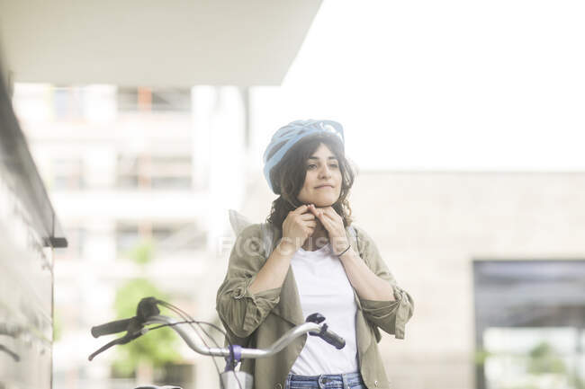 Woman standing by her bike putting on her bicycle helmet — Stock Photo