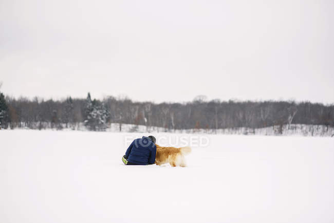 Homem sentado na neve com seu cão golden retriever — Fotografia de Stock