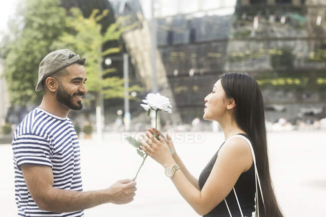 Man standing in city square giving his girlfriend a white rose — Stock Photo