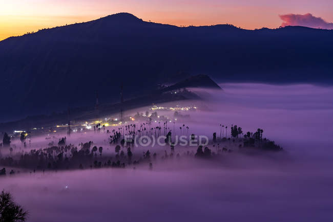 Low clouds engulfing Cemoro Lawang village during glorious sunrise at Bromo Tengger Semeru National Park in East Java Province, Indonesia. — Stock Photo