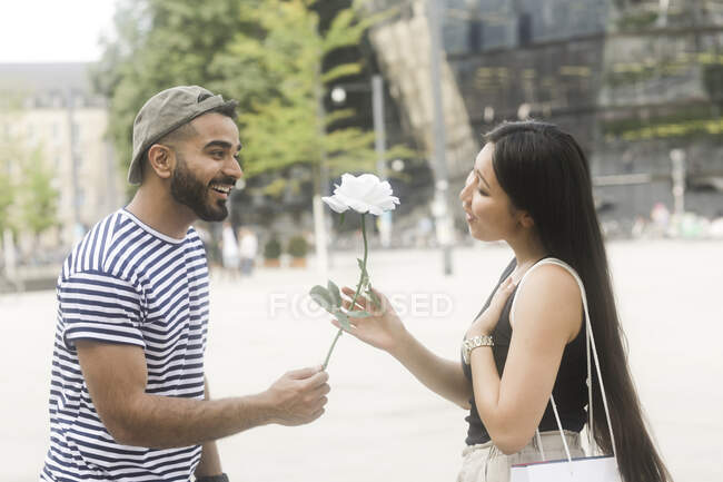 Man standing in city square giving his girlfriend a white rose — Stock Photo