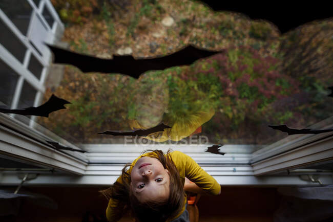 Над головою вимальовується дівчина, що стоїть біля вікна, прикрашеного зображенням кажанів для Хелловін, США. — стокове фото