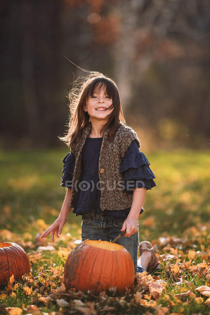Chica sonriente tallando una calabaza de Halloween en el jardín, Estados Unidos - foto de stock