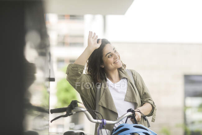 Retrato de uma mulher sorridente em pé ao lado de sua bicicleta acenando — Fotografia de Stock