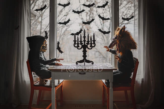 Two children in Halloween costumes sitting by a window doing a jigsaw puzzle, United States — Stock Photo