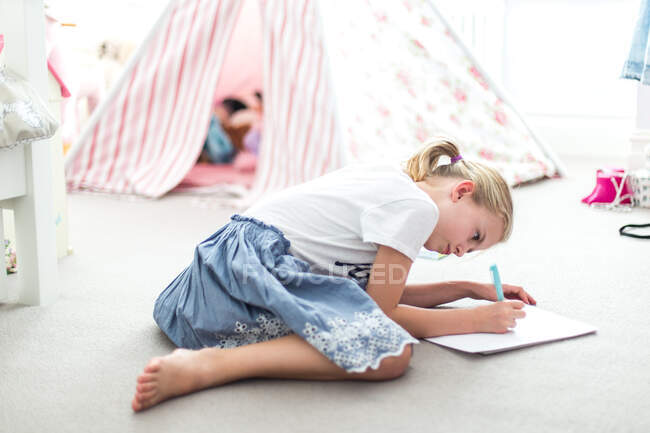 Girl sitting on the floor in her bedroom doing homework — Foto stock