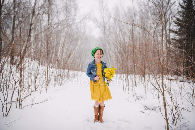 Fille debout dans la neige tenant un bouquet de fleurs — Photo de stock